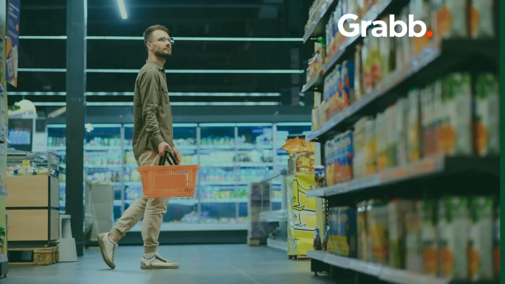 Shopper carrying an orange basket through a grocery aisle, looking toward shelf products