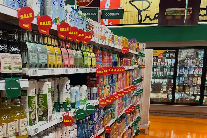 Grocery aisle with beverage products, sale tags and Non-GMO shelf labels