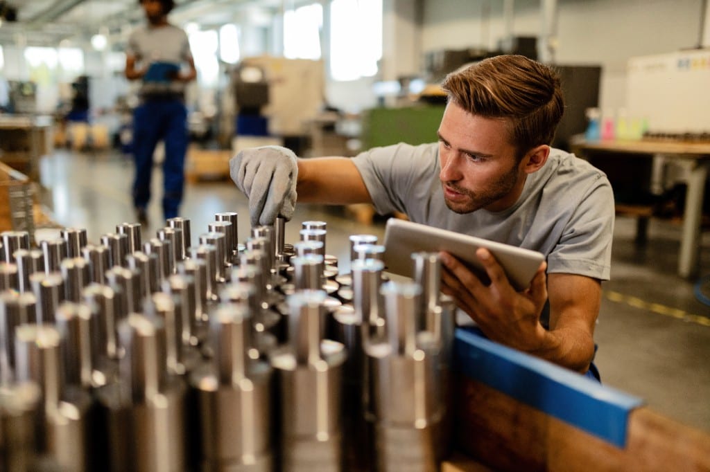 Manufacturer inspecting machined steel parts on the factory floor with a tablet before distribution